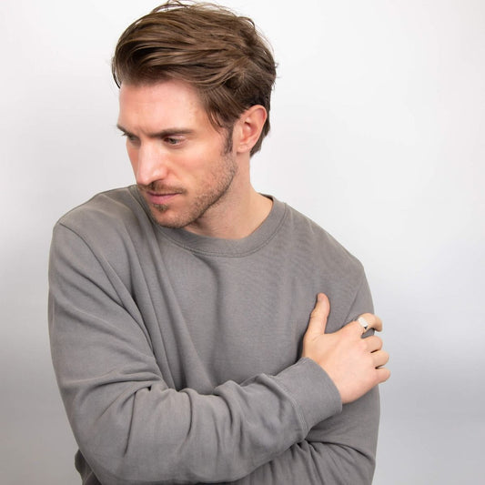 Uomo che indossa un anello chevalier quadrato in argento di BDG Accessories con maglione grigio